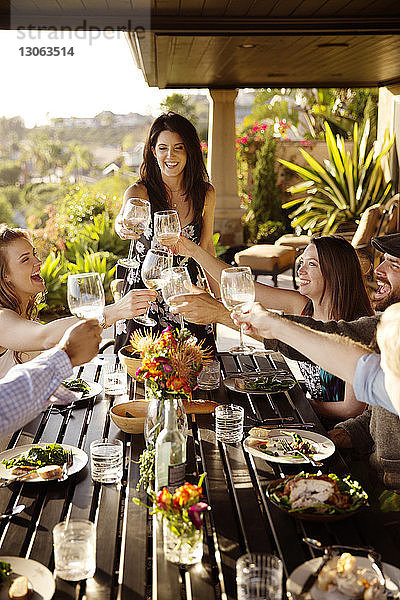 Glückliche Freunde stoßen am Esstisch auf der Veranda auf Weingläser an