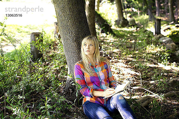 Frau schaut auf  während sie im Wald am Baumstamm sitzt