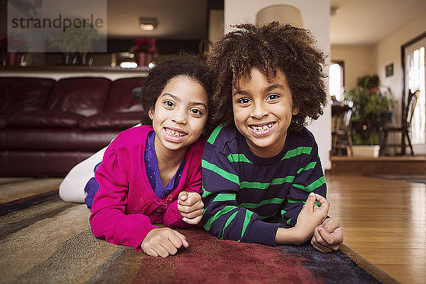 Porträt von glücklichen Geschwistern  die zu Hause auf dem Teppich liegen