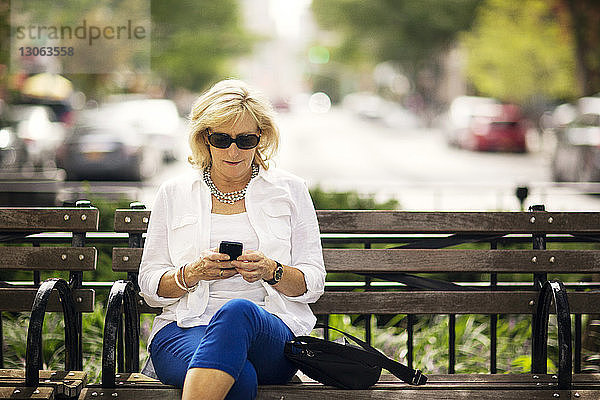 Frau benutzt Mobiltelefon  während sie auf einer Bank sitzt