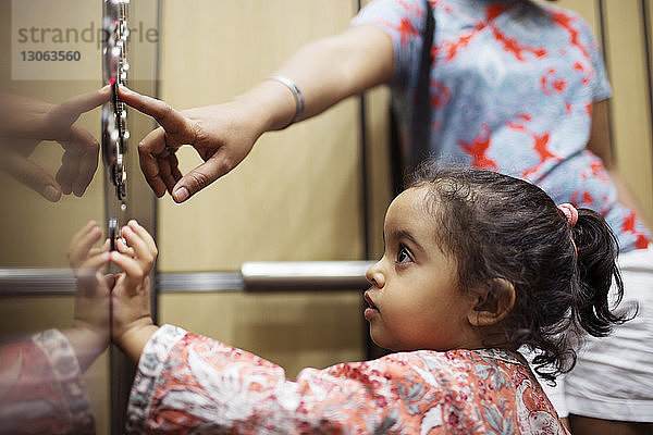 Frau drückt Druckknopf  während ihre Tochter in den Aufzug schaut