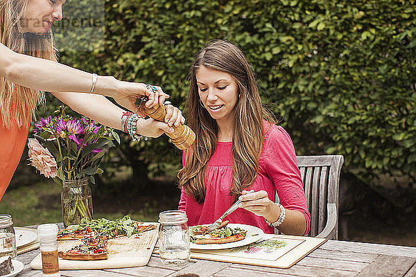 Frau mahlt Pfeffer auf Essen für einen Freund  während sie im Rasen am Tisch sitzt