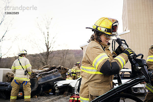 Weibliche Feuerwehrfrau schneidet Auto  während sie gegen den klaren Himmel steht