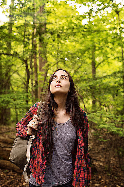 Frau mit Rucksack schaut im Wald stehend nach oben