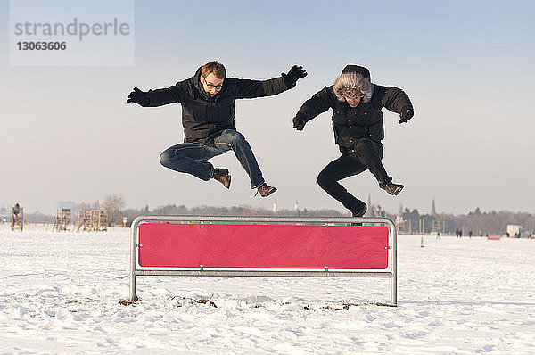 Glückliche Freunde springen über Hürde auf schneebedecktem Feld