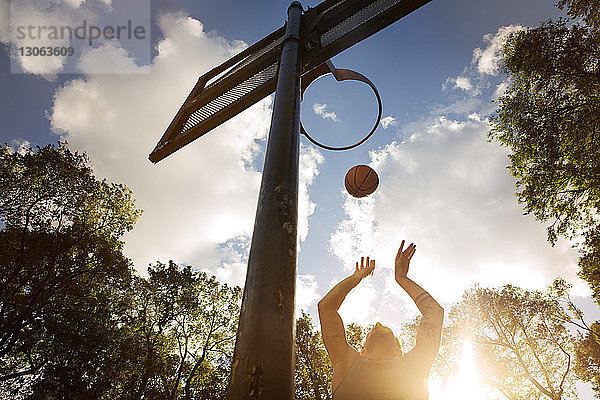 Niedrigwinkelansicht eines Basketball spielenden Athleten im Gericht gegen den Himmel