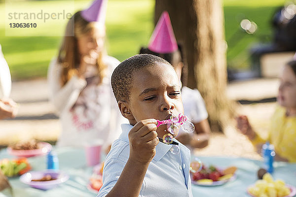Junge bläst Seifenblasen  während Freunde bei Geburtstagsfeier am Tisch essen
