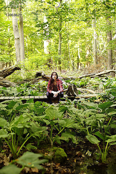 Frau schaut weg  während sie auf einem Steg im Wald sitzt