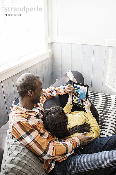 Hochwinkelansicht eines Paares  das auf einen Tablet-Computer schaut  während es auf dem Sofa sitzt