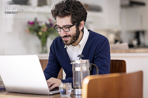 Mann benutzt Laptop-Computer  während er zu Hause am Tisch sitzt