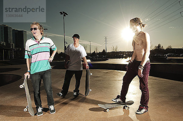 Freunde mit Skateboard auf der Sportrampe bei Sonnenuntergang