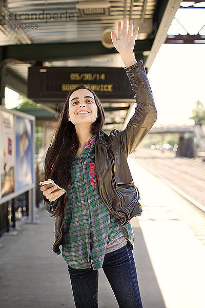 Lächelnde Frau winkt mit der Hand  während sie auf dem Bahnsteig steht
