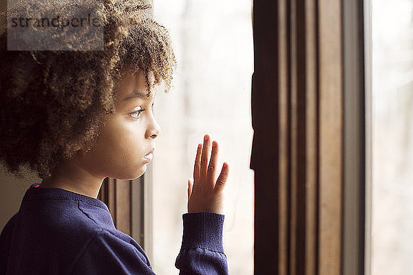 Nahaufnahme einer Seitenansicht eines nachdenklichen Jungen  der zu Hause durch ein Fenster schaut