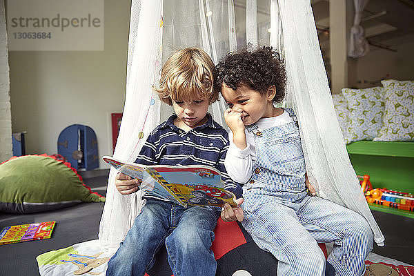 Freunde lesen Bilderbuch  während sie in der Kinderbetreuung auf einem Sitzsack sitzen