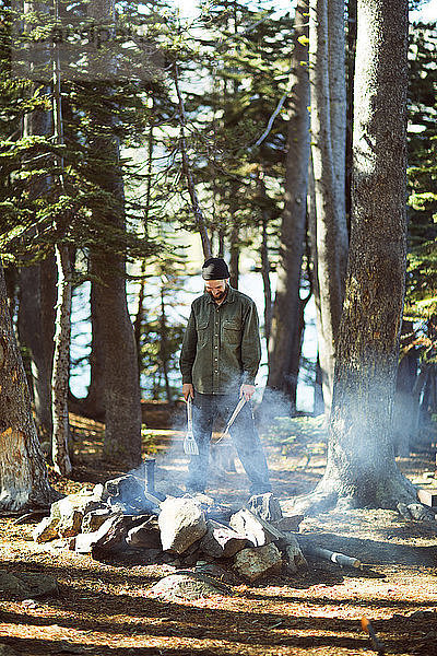 Glücklicher Mann steht am Lagerfeuer im Wald