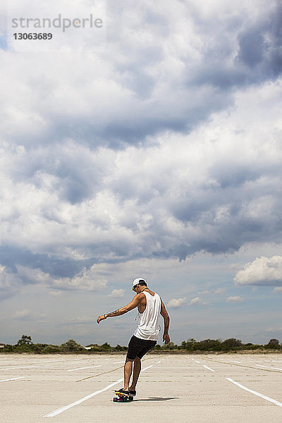 Rückansicht eines Mannes beim Skateboarden auf dem Feld vor bewölktem Himmel