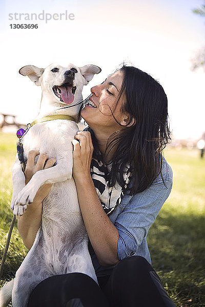 Glückliche Frau mit verspieltem Hund im Park gegen den Himmel
