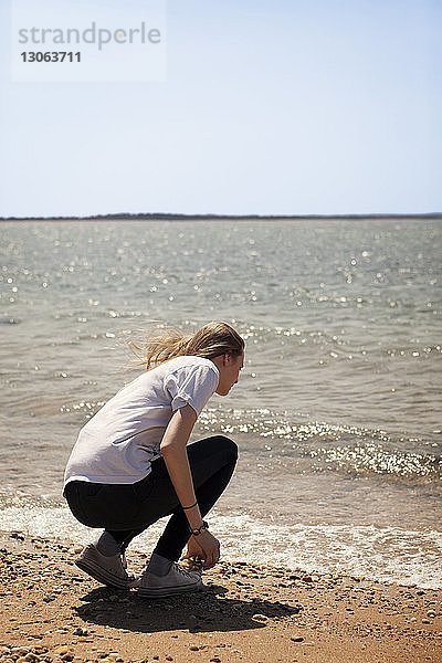 Rückansicht einer Frau  die am Strand am Ufer kauert