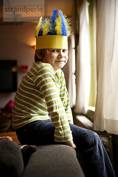 Seitenansicht Porträt eines lächelnden Jungen  der zu Hause einen Federhut trägt