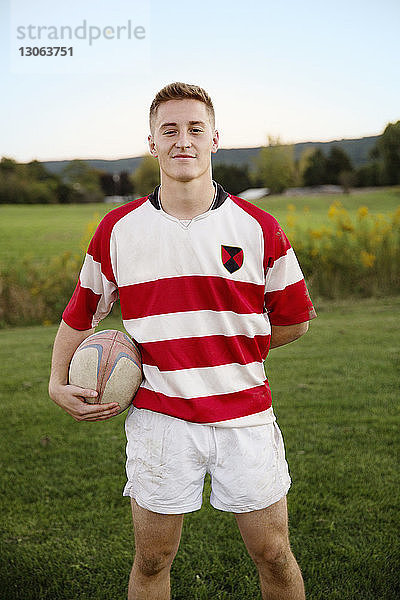 Porträt eines selbstbewussten Spielers  der den Rugbyball auf dem Feld gegen den klaren Himmel hält