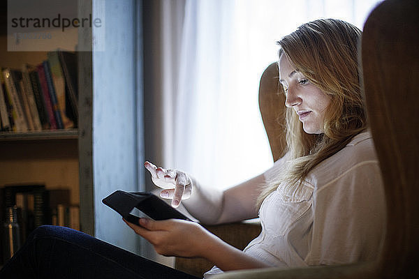 Frau benutzt Tablet-Computer  während sie zu Hause auf einem Sessel sitzt