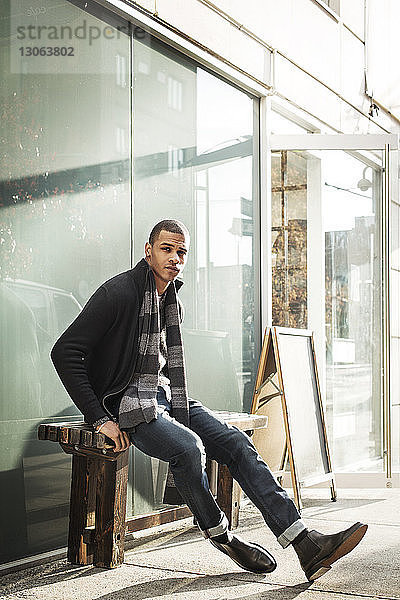 Porträt eines selbstbewussten Mannes  der auf einer Bank vor einem Café sitzt