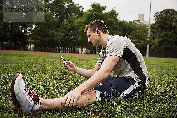 Mann benutzt Smartphone  während er im Park auf dem Feld sitzt