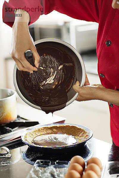 Mittelteil einer Frau  die geschmolzene Schokolade in einen Behälter gießt