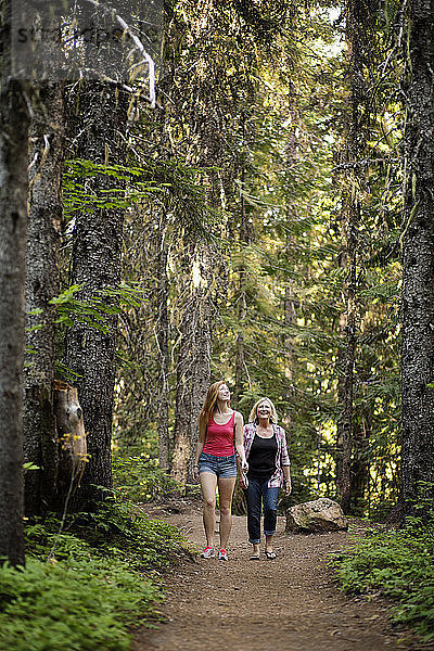 Glückliche Mutter und Tochter gehen auf einem Pfad zwischen Bäumen im Wald