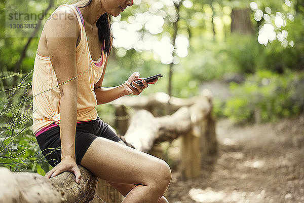 Frau im Mittelteil  die ein Smartphone benutzt  während sie im Park auf einem Geländer sitzt