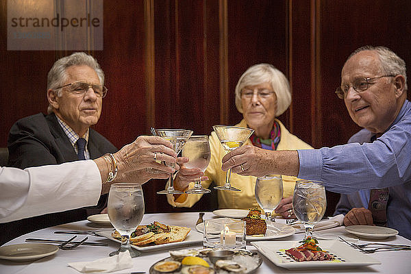 Ältere Freunde stoßen im Restaurant auf Martini-Gläser an