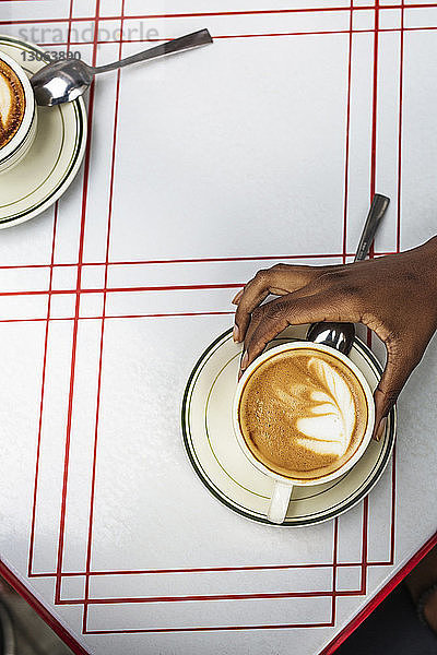 Ausschnitt eines Cappuccino in der Hand haltenden Cafes auf dem Bürgersteig