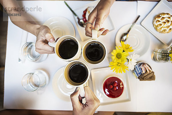 Ausgeschnittenes Bild von Freunden  die mit Kaffeetassen am Tisch im Restaurant anstoßen