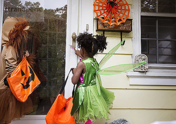 Kinder in Halloween-Kostümen  die während einer Süßes-oder-Saures-Tour an der Tür stehen