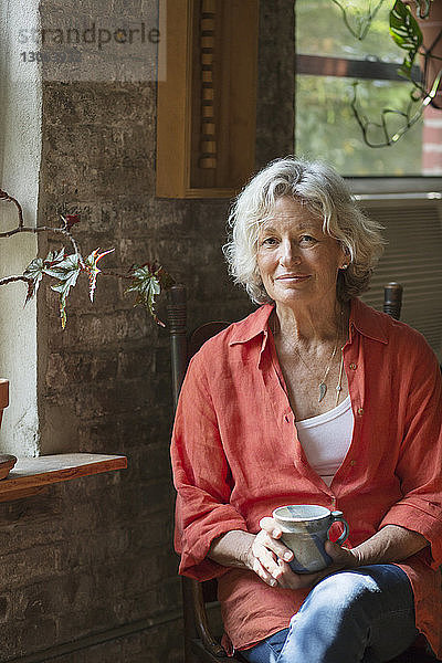 Porträt einer lächelnden Frau  die zu Hause sitzt und eine Kaffeetasse hält