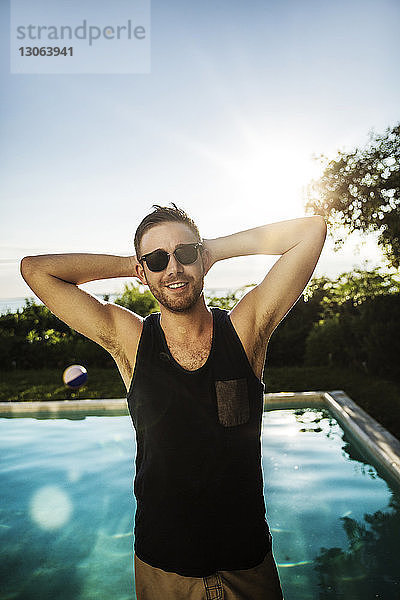 Mann mit Händen hinter dem Kopf steht im Hinterhof am Pool