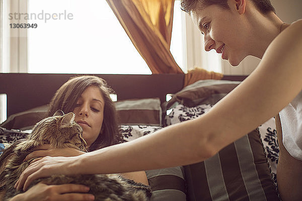 Frauen schauen der Katze zu  während sie sich zu Hause im Bett entspannen