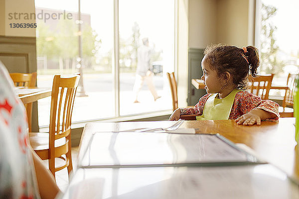 Mädchen trägt Babylätzchen  während sie im Restaurant am Tisch sitzt