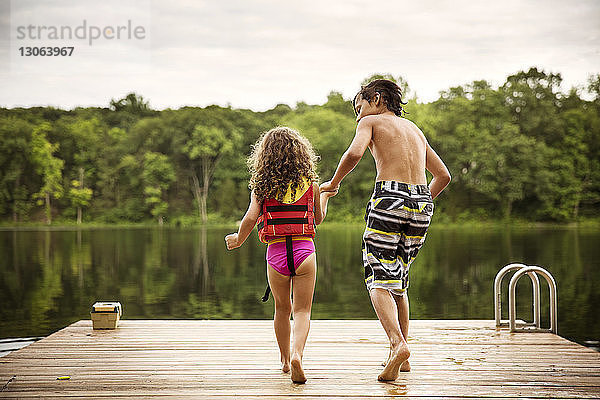 Rückansicht eines Jungen mit einer Schwester  der am Dock gegen den See läuft