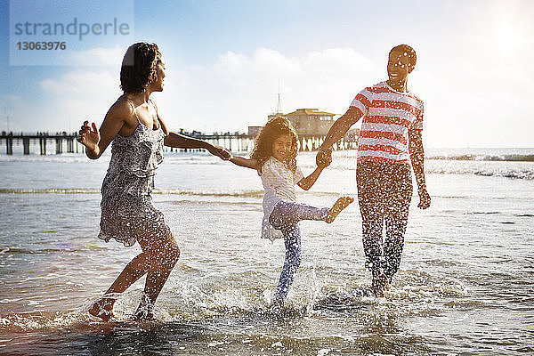Glückliche Familie genießt am Strand gegen den Himmel