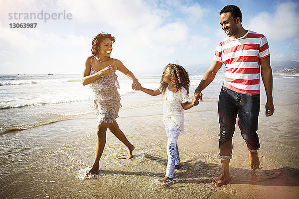 Glückliche Familie mit Händchenhalten beim Strandspaziergang am Ufer
