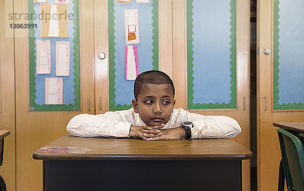 Gelangweilter Junge sitzt am Schreibtisch im Klassenzimmer