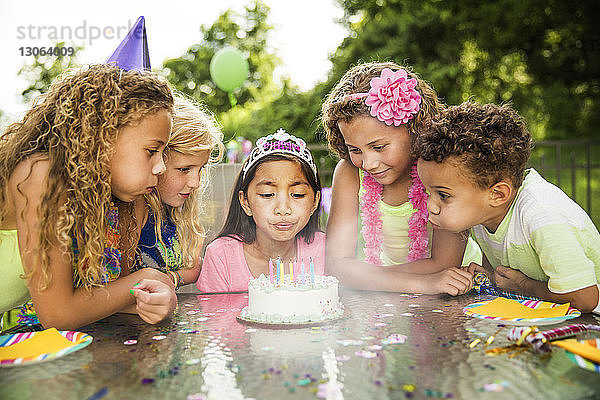 Mädchen bläst Geburtstagskuchenkerzen aus  während sie mit Freunden im Garten steht
