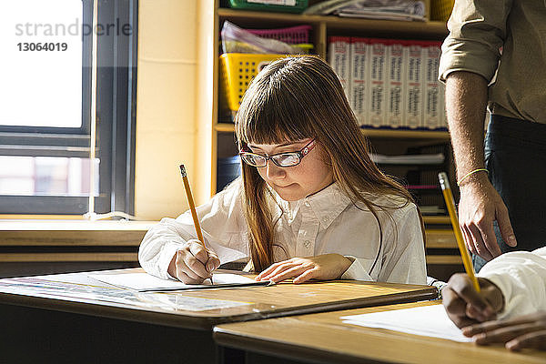Mädchen schreibt auf Papier  während sie im Klassenzimmer am Schreibtisch sitzt