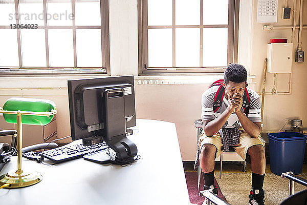 Angespannter Teenager sitzt auf Stuhl im Büro des Schulleiters in der Schule