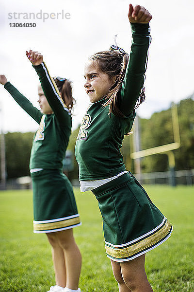 Glückliche Cheerleader tanzen auf dem Feld gegen den Himmel