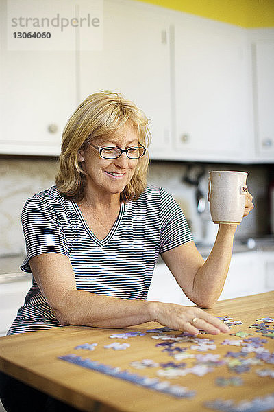 Frau hält Tasse beim Puzzlespielen zu Hause