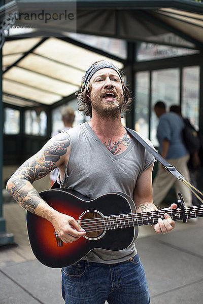 Mann singt beim Gitarrespielen auf der Straße