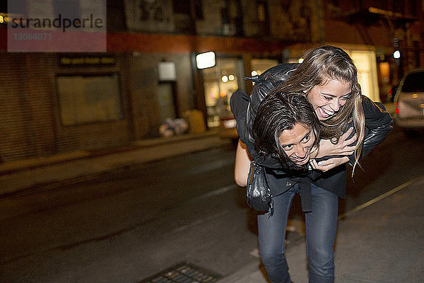 Glücklicher Mann nimmt seine Freundin huckepack  während er nachts auf einem Fußweg geht