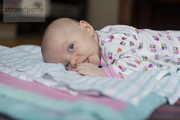 Süßes Baby-Mädchen schaut weg  während es auf einer Decke liegt